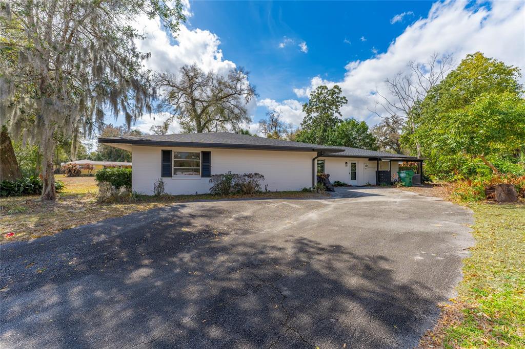 A white, single-story house with a dark roof and a large asphalt driveway — 715 EASTOVER CIR CIRCLE, DELAND, FL