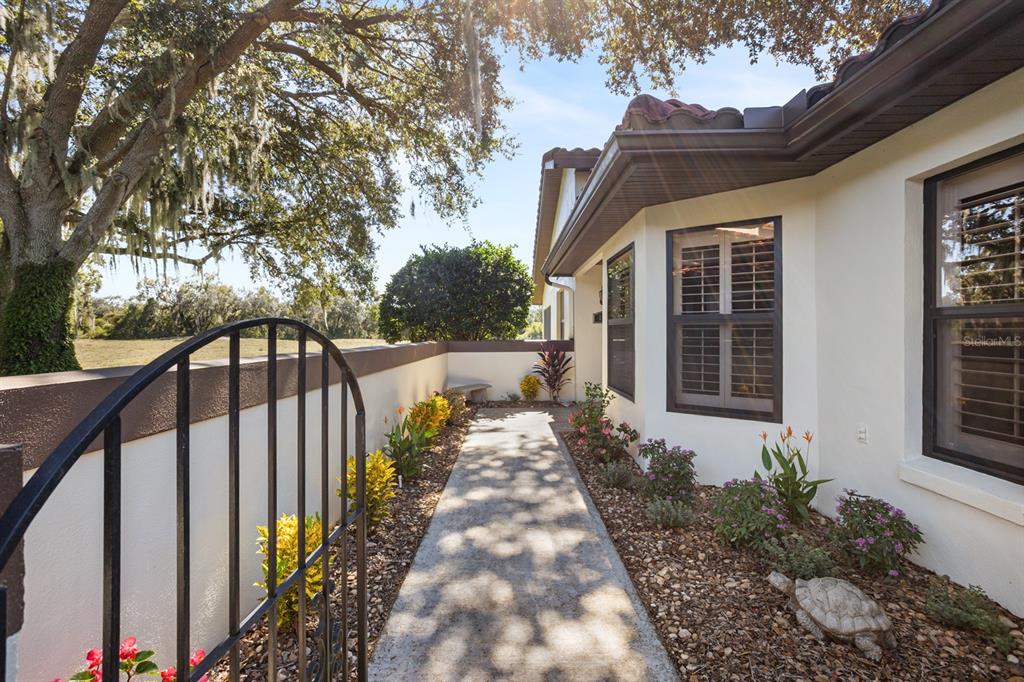 A concrete walkway leads to a house entrance past a black metal gate and landscaping — 138 STRATFORD COURT, HAINES CITY, FL