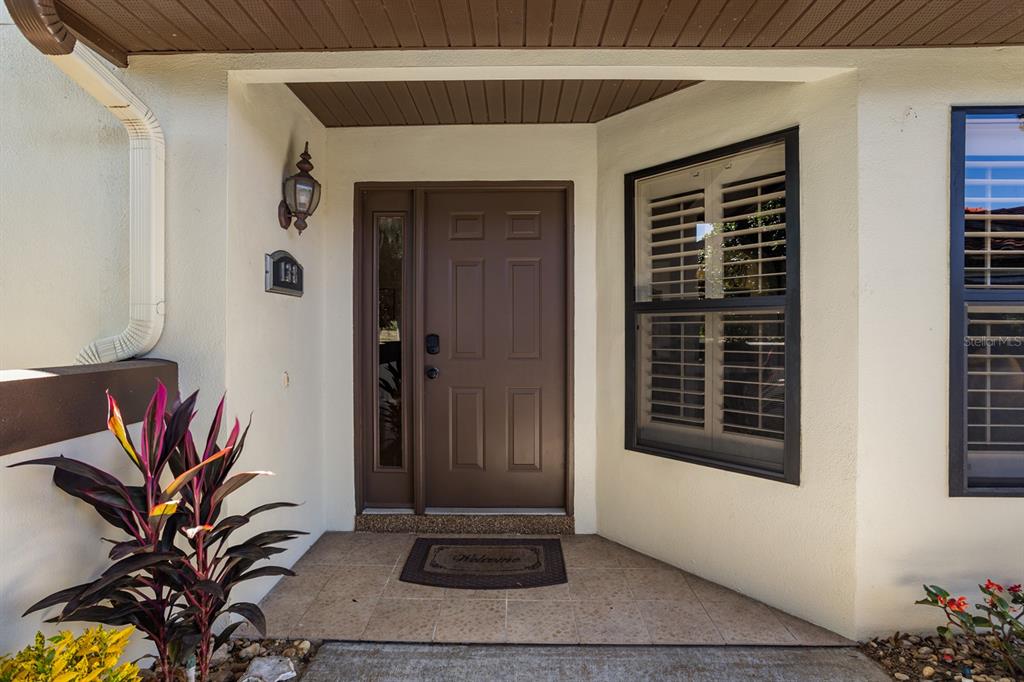 The exterior entrance features a brown front door, a side window, and a tiled porch — 138 STRATFORD COURT, HAINES CITY, FL