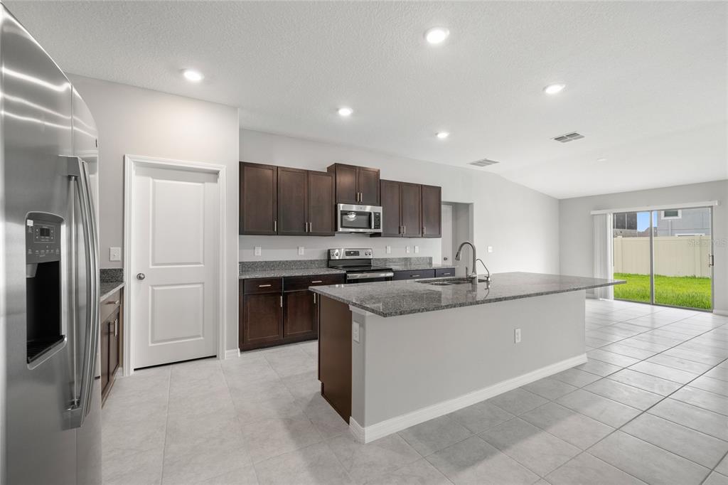 A kitchen with dark wood cabinets, granite countertops, a center island, and light tile flooring — 16612 CARLTON POND STREET, WIMAUMA, FL