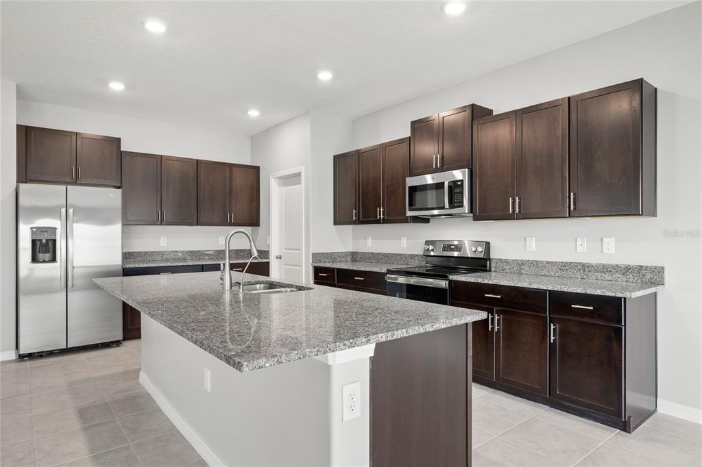 A kitchen with dark wood cabinets, granite countertops, stainless steel appliances, and a central island — 16612 CARLTON POND STREET, WIMAUMA, FL
