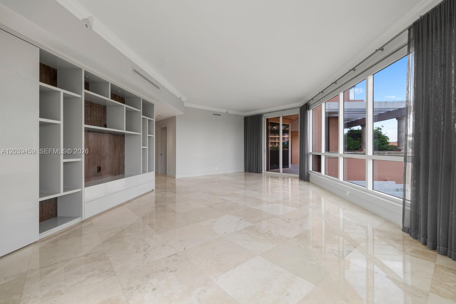 A spacious living room features light marble flooring, a large built-in shelving unit, and floor-to-ceiling windows — 10 Edgewater Dr # 4H, Coral Gables FL 33133, CORAL GABLES, FL