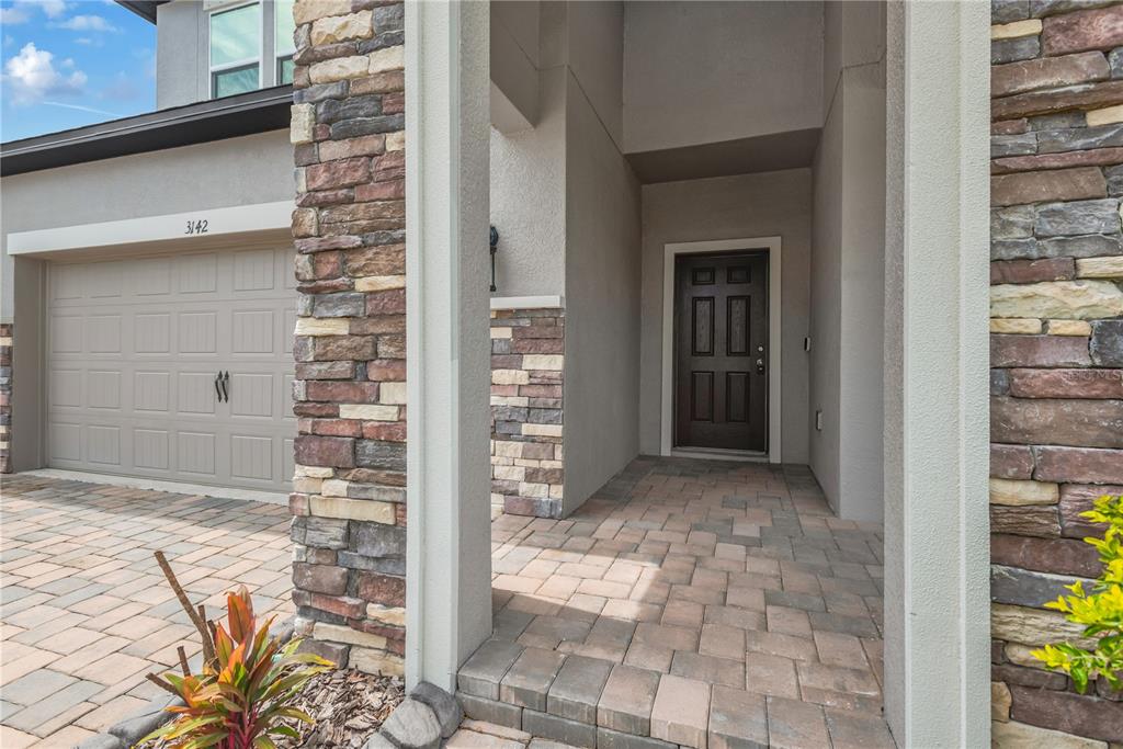 A paved walkway leads to a dark front door beside a stone-accented garage — 3142 MARINE GRASS DRIVE, WIMAUMA, FL