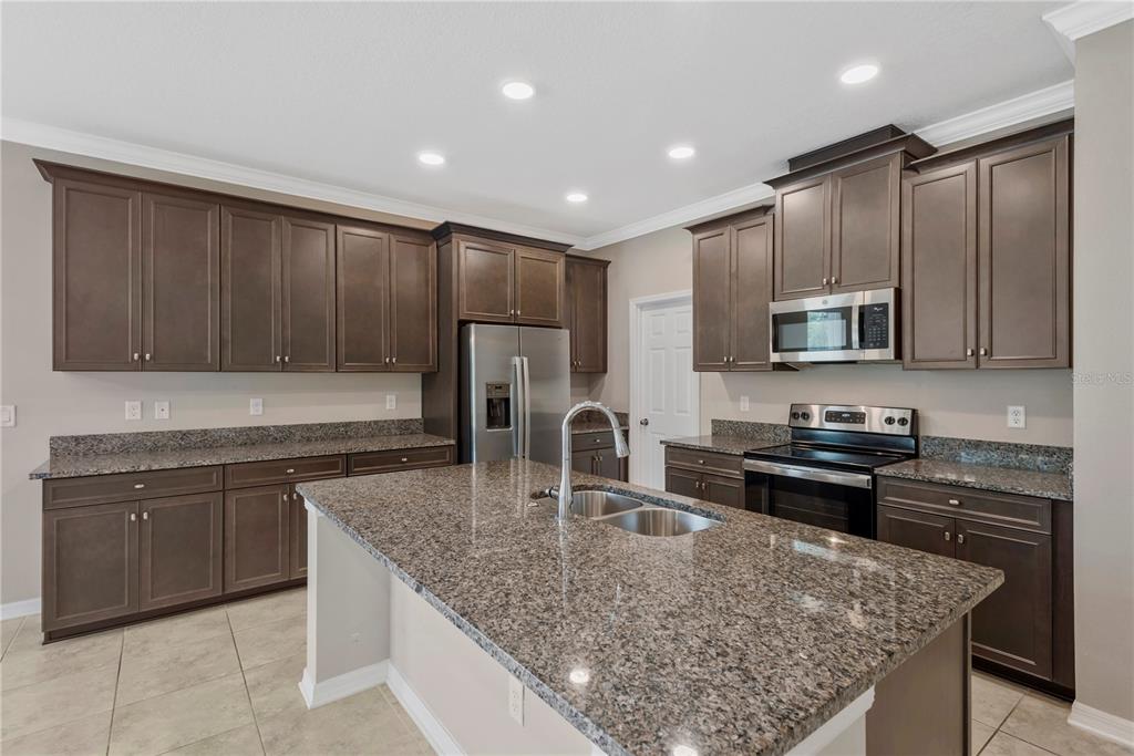 A kitchen with dark wood cabinets, granite countertops, a center island, and stainless steel appliances — 3142 MARINE GRASS DRIVE, WIMAUMA, FL