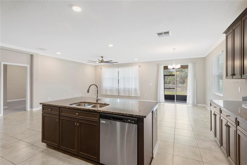 A kitchen with a granite-topped island, stainless steel dishwasher, and dark wood cabinetry — 3142 MARINE GRASS DRIVE, WIMAUMA, FL