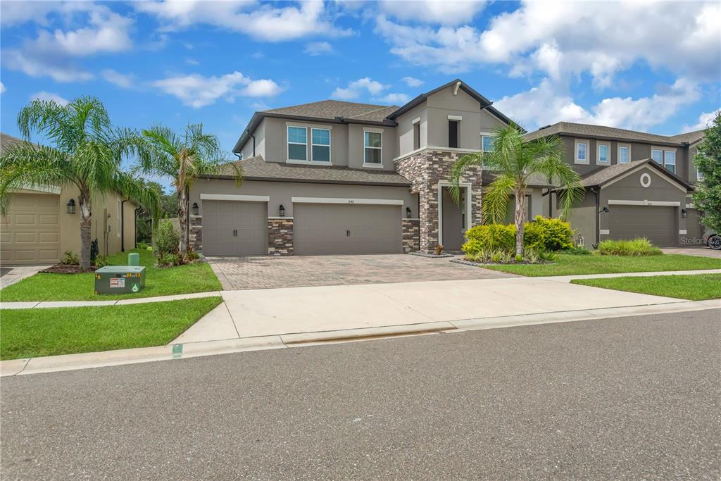 A two-story suburban house with a three-car garage, stone accents, and palm trees — 3142 MARINE GRASS DRIVE, WIMAUMA, FL