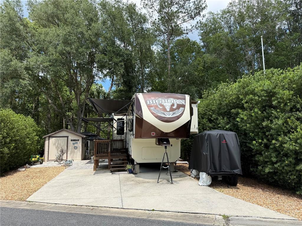 A Bighorn fifth-wheel RV is parked on a concrete pad next to a small shed — 2853 NE 104TH TERRACE, SILVER SPRINGS, FL