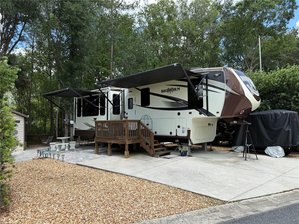 A large Bighorn fifth-wheel RV with an attached wooden deck sits on a paved lot — 2853 NE 104TH TERRACE, SILVER SPRINGS, FL