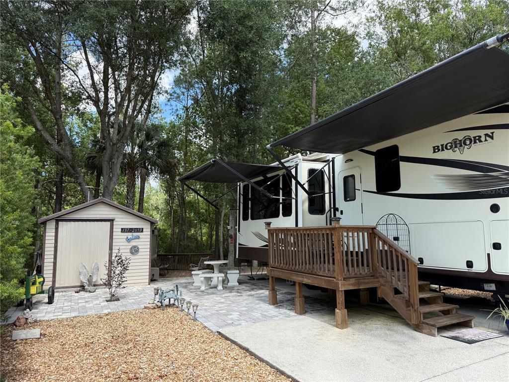 A Bighorn fifth-wheel RV is parked next to a storage shed on a paved patio — 2853 NE 104TH TERRACE, SILVER SPRINGS, FL