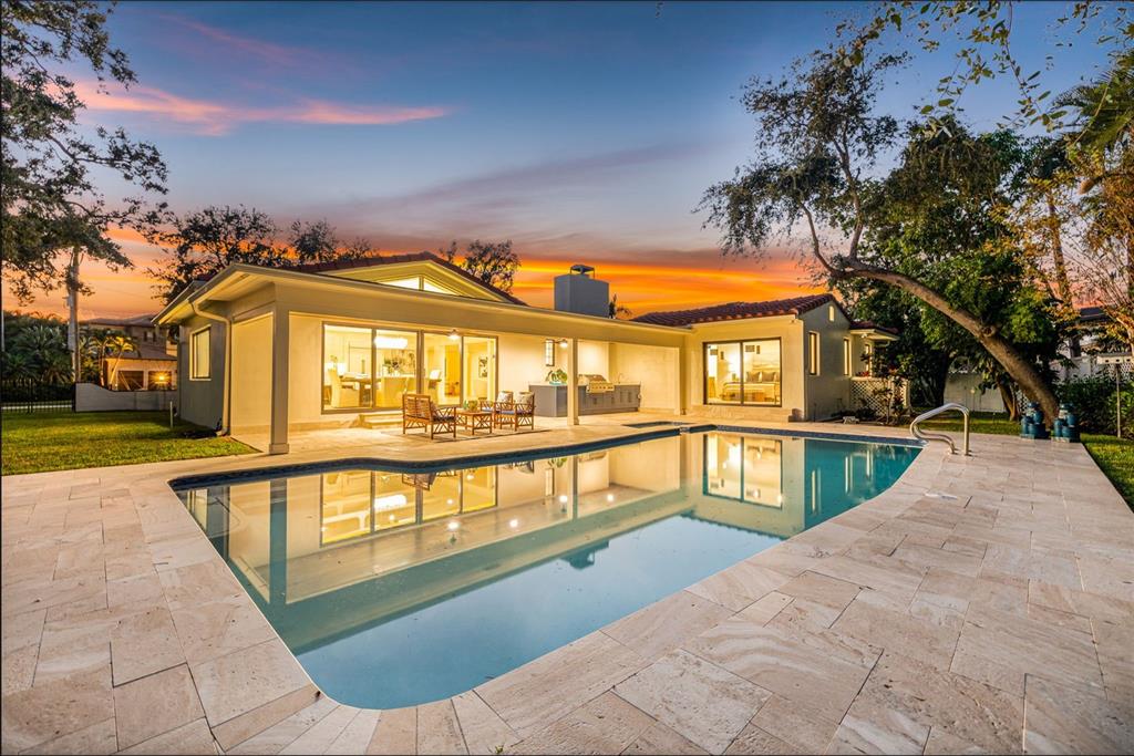 A backyard with a swimming pool, stone patio, and a single-story house at sunset — 1222 BRIGHTWATERS BOULEVARD NE, ST PETERSBURG, FL