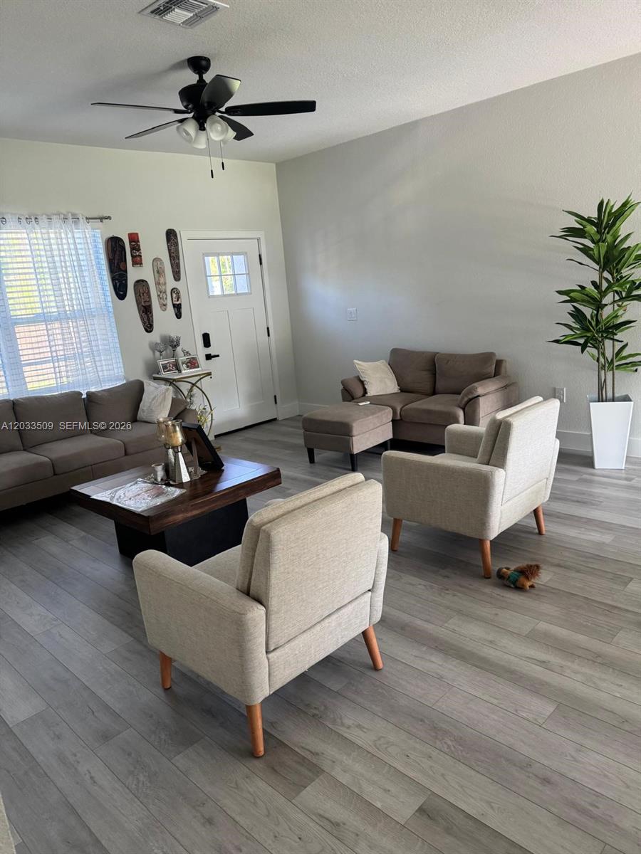 A living room features gray wood-look flooring, a ceiling fan, and multiple seating areas — 1398 SW Breezy Point Drive, Ocala FL 34431, OCALA, FL