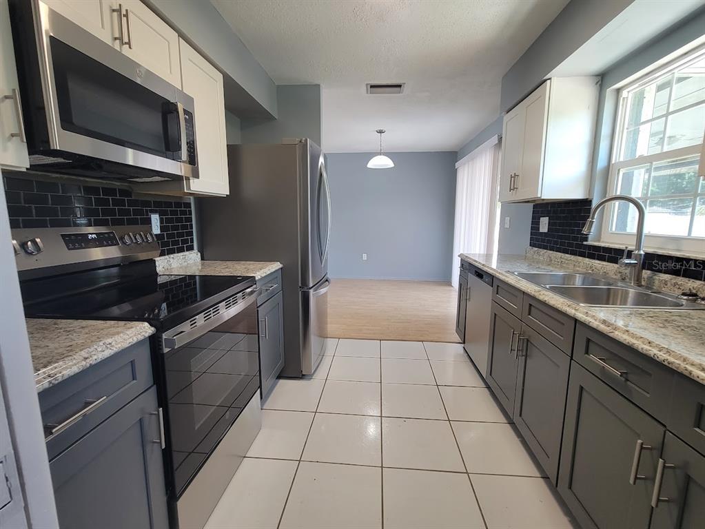 A kitchen with grey lower cabinets, white upper cabinets, stainless steel appliances, and tiled floors — 22329 NIAGARA AVENUE, PORT CHARLOTTE, FL