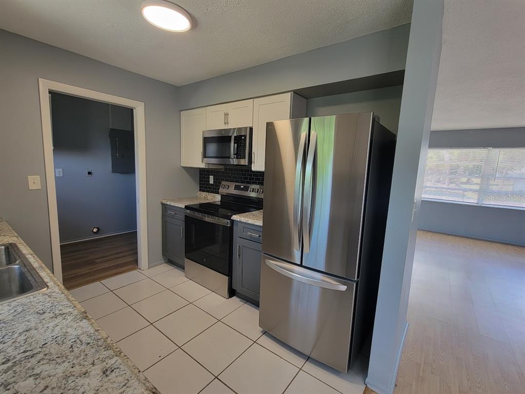A kitchen features stainless steel appliances, white upper cabinets, gray lower cabinets, and tile flooring — 22329 NIAGARA AVENUE, PORT CHARLOTTE, FL