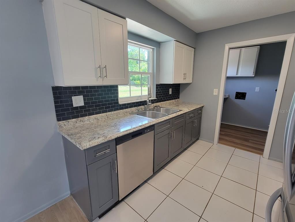 A kitchen features gray lower cabinets, white upper cabinets, granite countertops, and a black backsplash — 22329 NIAGARA AVENUE, PORT CHARLOTTE, FL