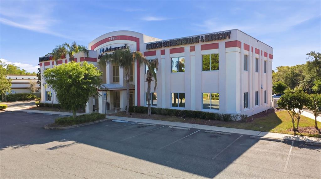 A two-story commercial building with a parking lot and palm trees under a blue sky — 1690 DUNLAWTON AVENUE UNIT 130, PORT ORANGE, FL