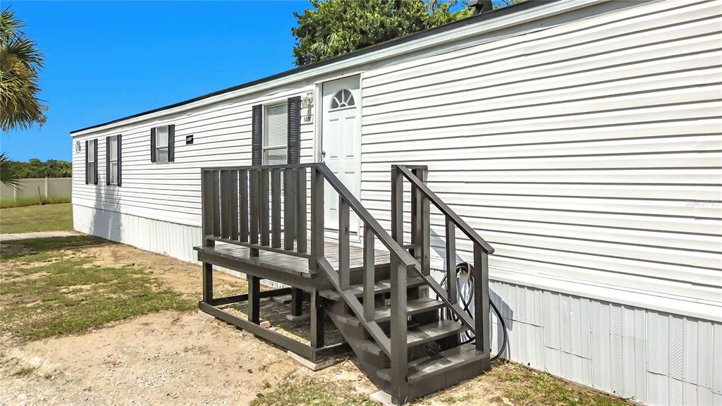 A white mobile home exterior features a dark wooden deck and stairs leading to a door — 1406 FINNEY ROAD, DAVENPORT, FL
