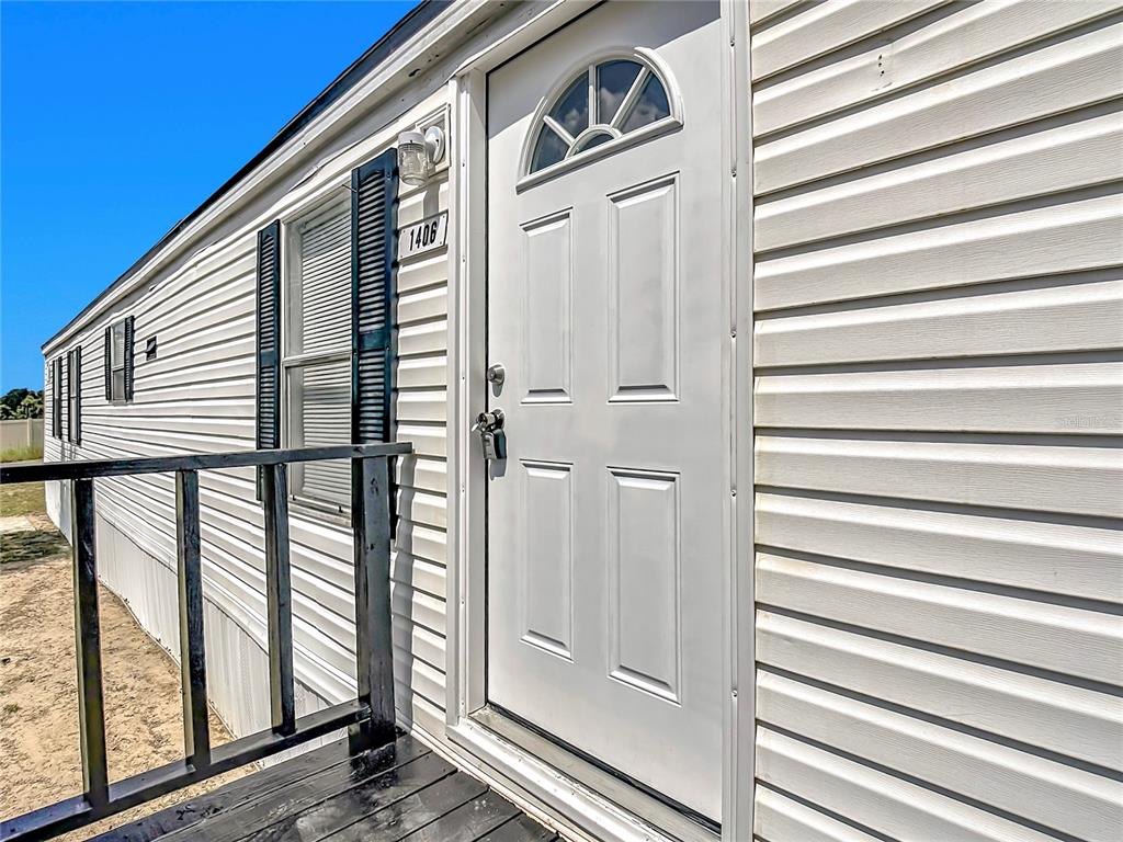 A white exterior wall with horizontal siding, a front door, and a black porch railing — 1406 FINNEY ROAD, DAVENPORT, FL