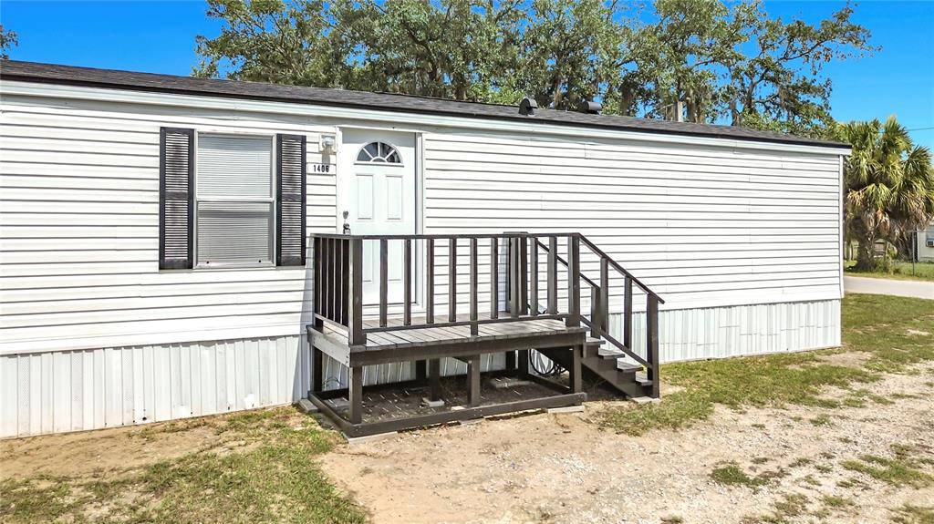 A white mobile home exterior features a dark wooden deck with stairs and a door — 1406 FINNEY ROAD, DAVENPORT, FL