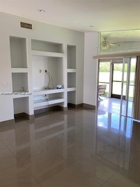 A living room features white built-in shelving, glossy tile flooring, and a sliding glass door — 504 Woodgate Cir # C, Sunrise FL 33326, SUNRISE, FL