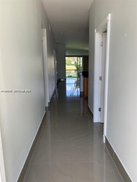 A hallway with light gray walls and glossy tile flooring leads toward a glass sliding door — 504 Woodgate Cir # C, Sunrise FL 33326, SUNRISE, FL