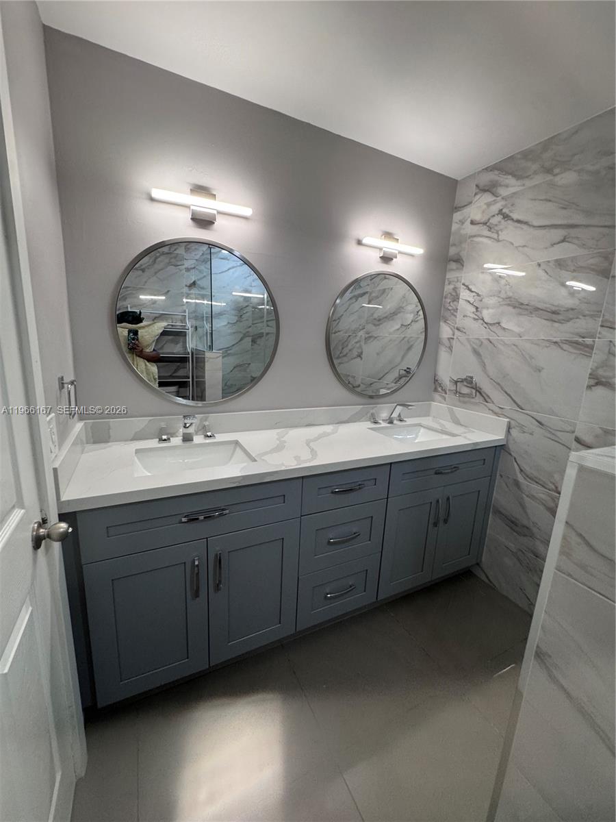 A bathroom features a double vanity with gray cabinets, white countertops, and two round mirrors — 504 Woodgate Cir # C, Sunrise FL 33326, SUNRISE, FL