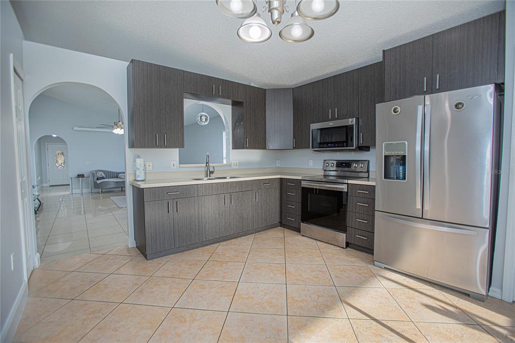 A kitchen features dark wood-grain cabinets, stainless steel appliances, and light-colored tile flooring — 659 CALADESI TRAIL, ORLANDO, FL