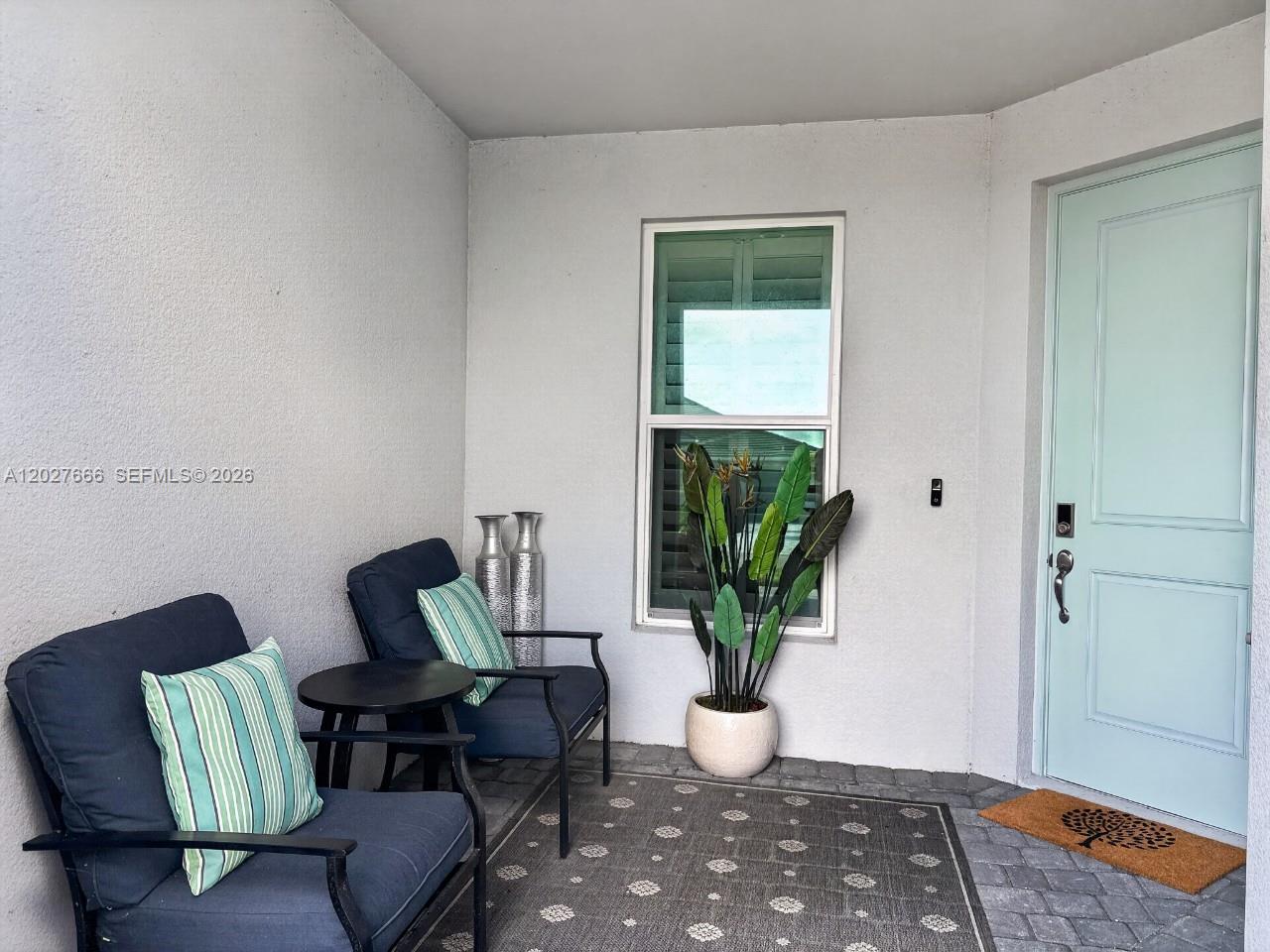 A covered entryway features two chairs, a small table, a potted plant, and a door — NAPLES, FL