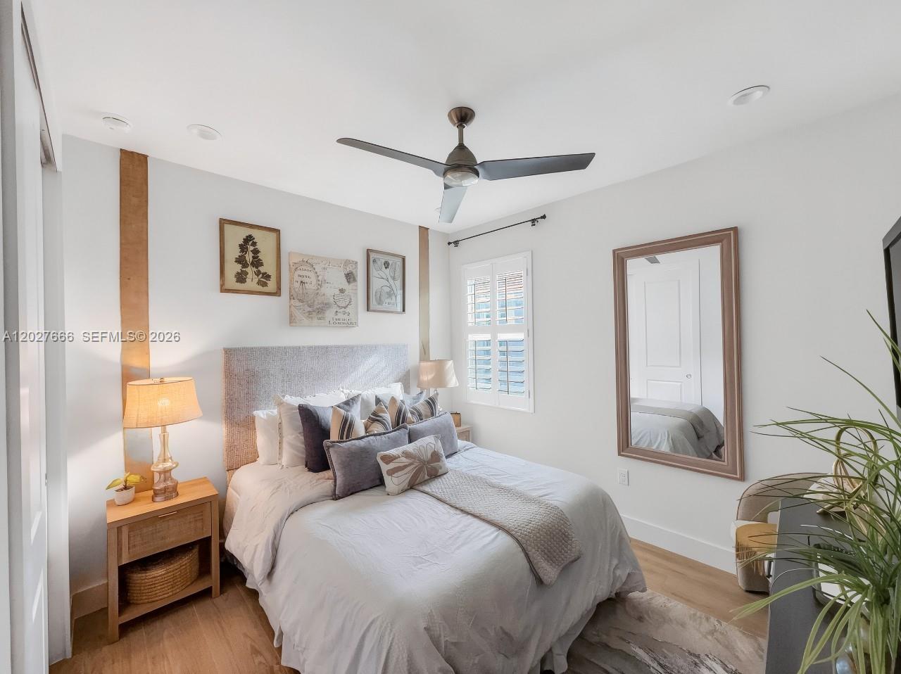A bedroom features a bed with a gray headboard, wood-toned accents, and a large wall mirror — NAPLES, FL