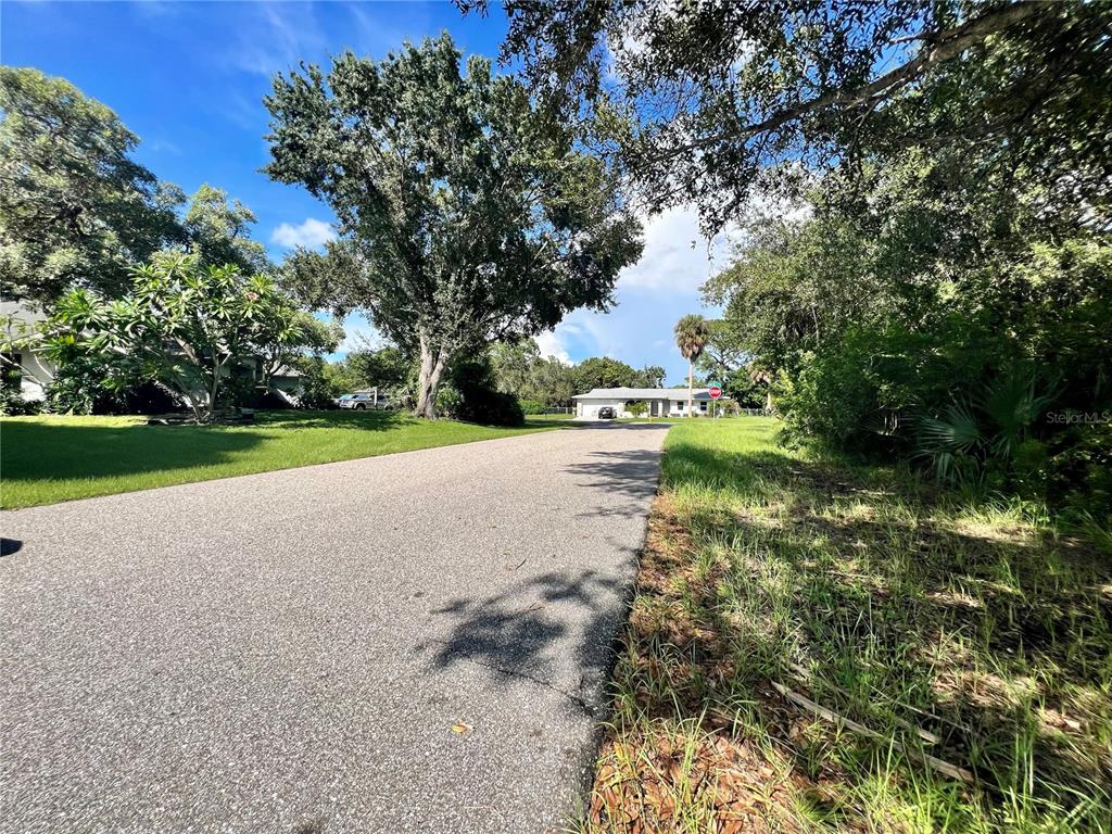 A paved road leads toward a single-story house surrounded by mature trees and lush vegetation — 5542 EYERLY TERRACE, PORT CHARLOTTE, FL