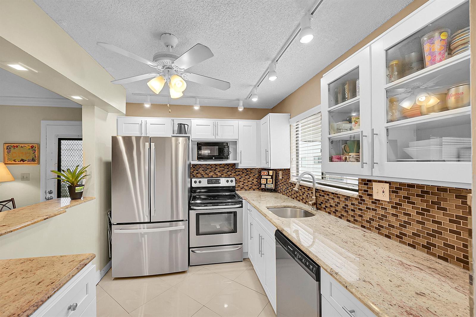 A kitchen features white cabinets, stainless steel appliances, granite countertops, and a brown tile backsplash — 15108 Ashland Drive # 198, Delray Beach FL 33484, DELRAY BEACH, FL