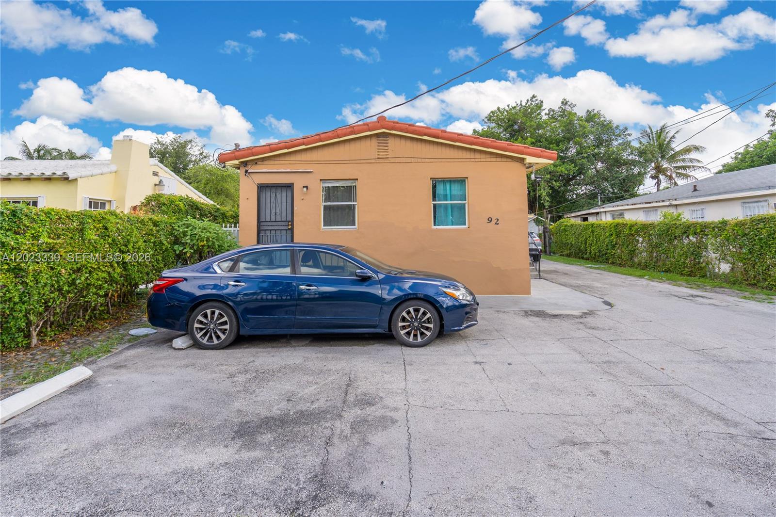 A tan, single-story house with a red tile roof sits behind a blue sedan — 94 NW 69th St, Miami FL 33150, MIAMI, FL