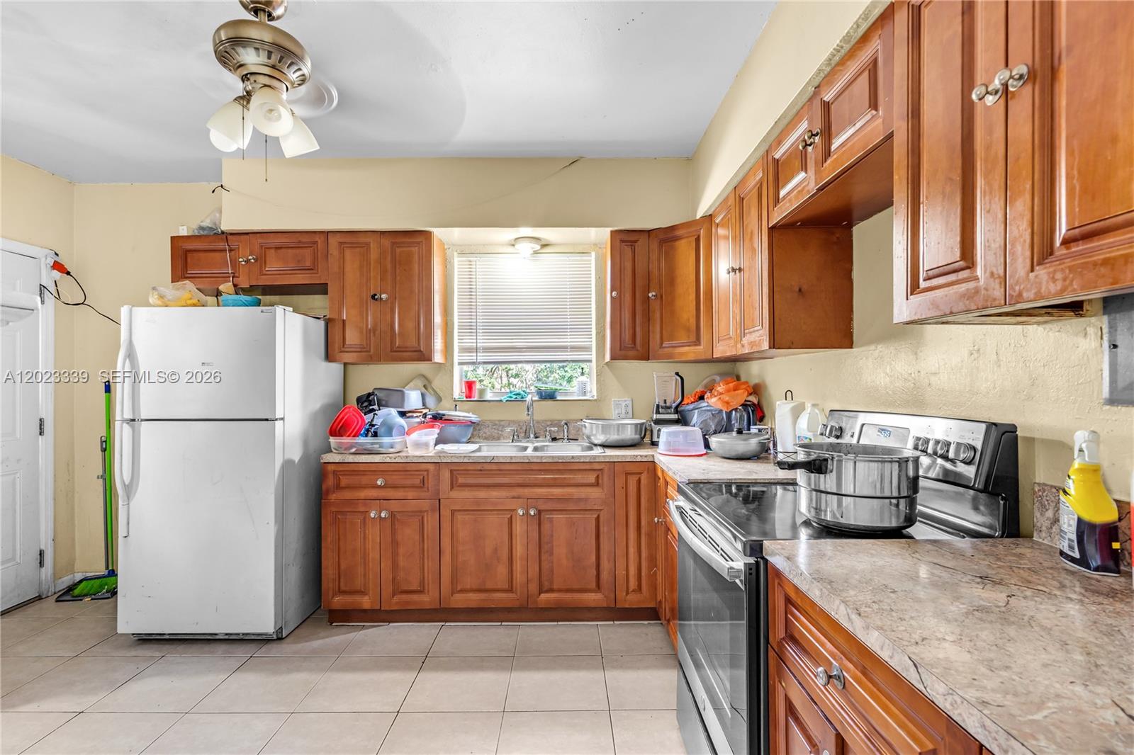 A kitchen features wood cabinets, a white refrigerator, a stainless steel stove, and tile flooring — 94 NW 69th St, Miami FL 33150, MIAMI, FL