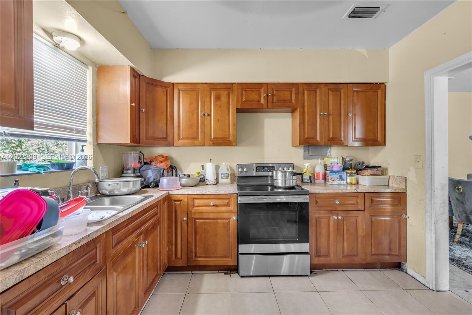 A kitchen features wood cabinets, a stainless steel stove, and light-colored tile flooring — 94 NW 69th St, Miami FL 33150, MIAMI, FL