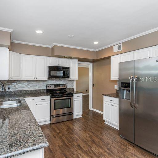 A kitchen features white cabinets, granite countertops, stainless steel appliances, and wood-look flooring — 2608 OAKWOOD DRIVE, LARGO, FL