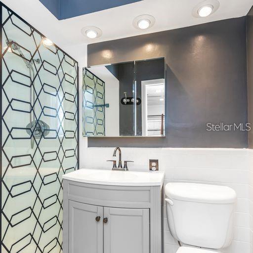 A bathroom features a gray vanity, a toilet, and a shower with a geometric patterned screen — 2608 OAKWOOD DRIVE, LARGO, FL