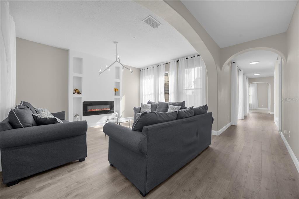 A living room features a fireplace, gray sofas, light wood flooring, and an arched hallway — 9657 MOSS ROSE WAY, ORLANDO, FL
