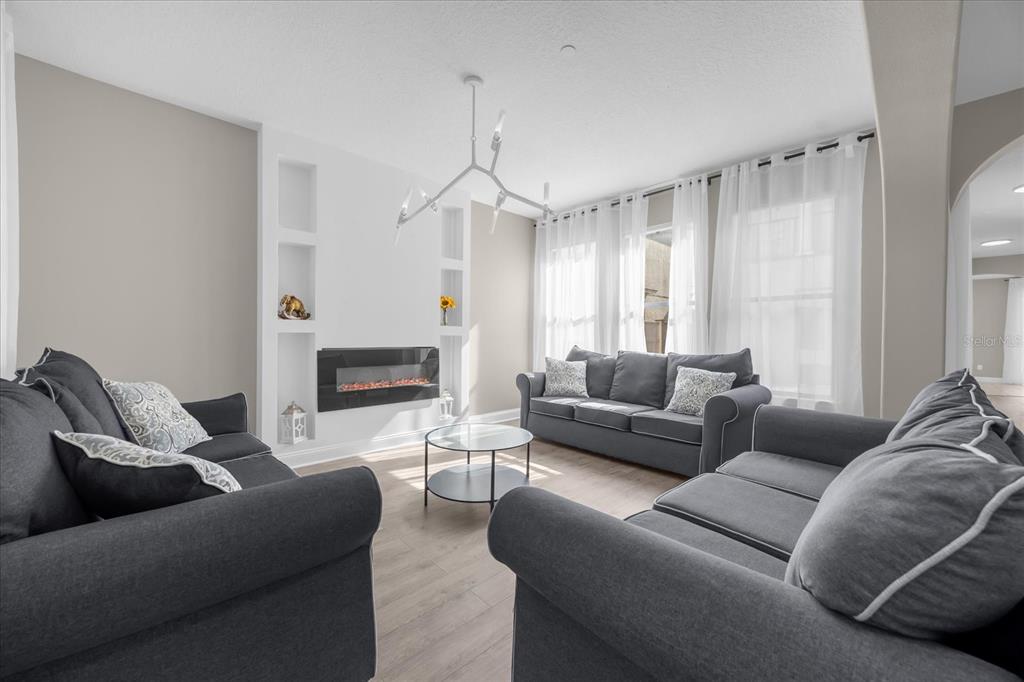 A living room with gray sofas, a wall-mounted fireplace, and a modern chandelier — 9657 MOSS ROSE WAY, ORLANDO, FL