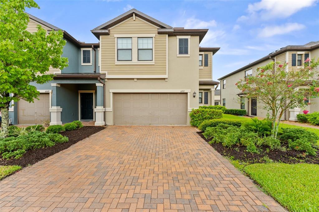A two-story suburban home features a brick paver driveway, a two-car garage, and landscaping — 16912 RED BRICK LANE, LAND O LAKES, FL