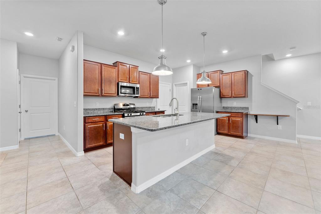 A kitchen with wood cabinets, granite countertops, a central island, and stainless steel appliances — 16912 RED BRICK LANE, LAND O LAKES, FL