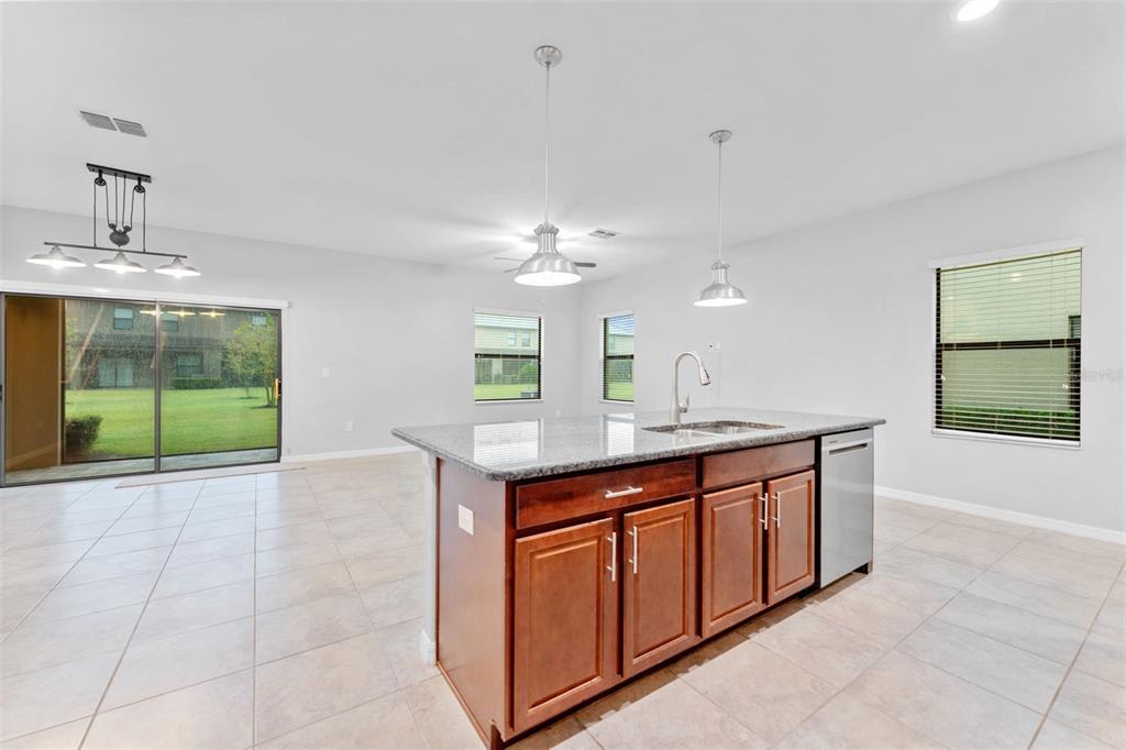 A kitchen island with dark wood cabinets and granite countertops sits in an open-concept room — 16912 RED BRICK LANE, LAND O LAKES, FL