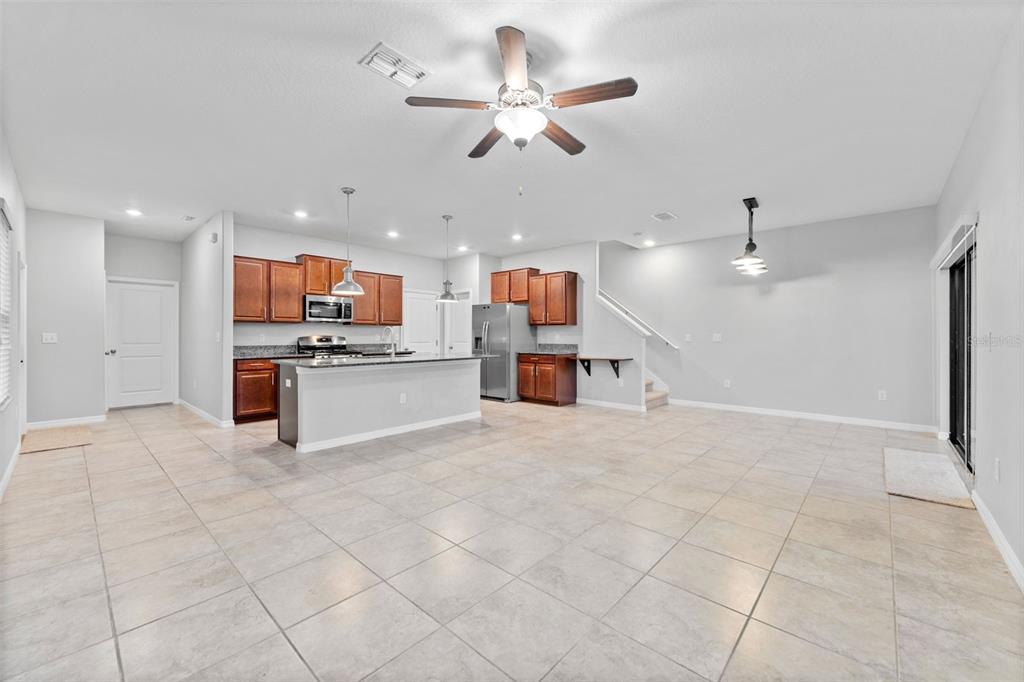 An open-concept kitchen with wood cabinets and a central island overlooks a tiled living area — 16912 RED BRICK LANE, LAND O LAKES, FL