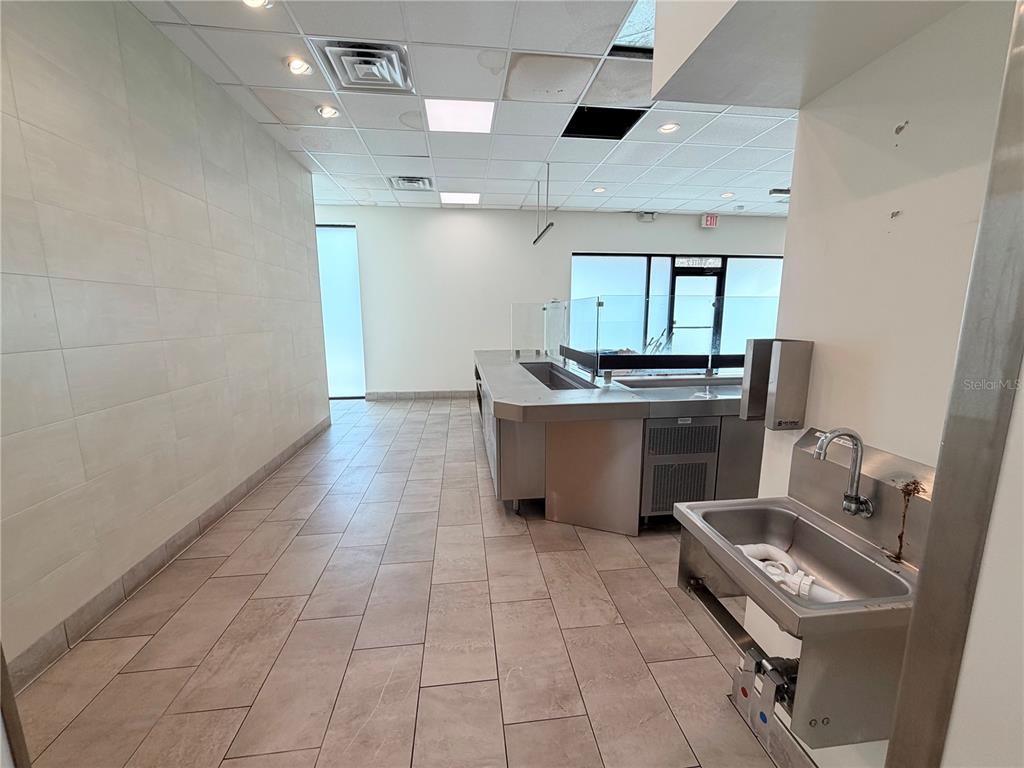A commercial kitchen space features a stainless steel counter, a utility sink, and tiled flooring — 6011 SE ABSHIER BOULEVARD, BELLEVIEW, FL