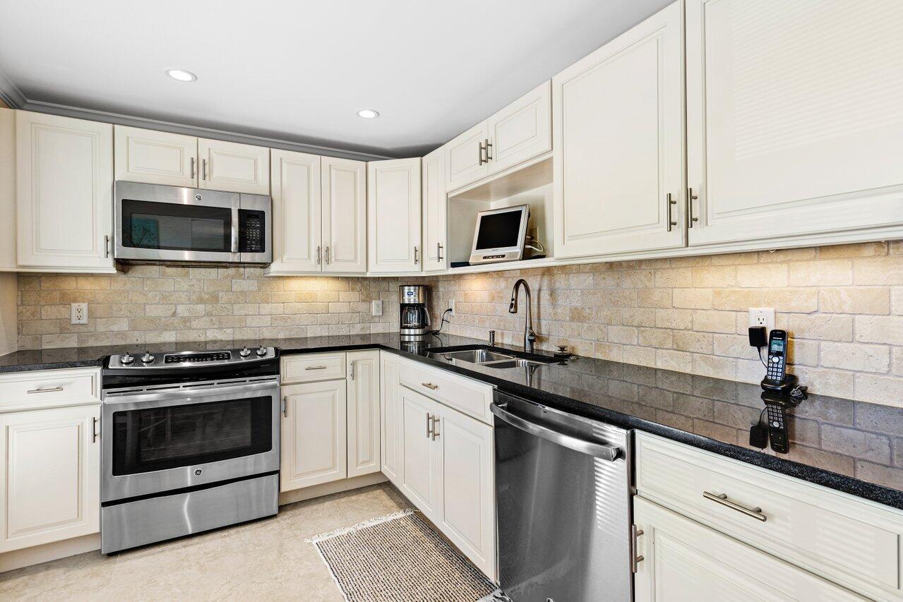 A kitchen with white cabinets, stainless steel appliances, black countertops, and a stone tile backsplash — 4643 Kittiwake Court, Boynton Beach FL 33436, BOYNTON BEACH, FL