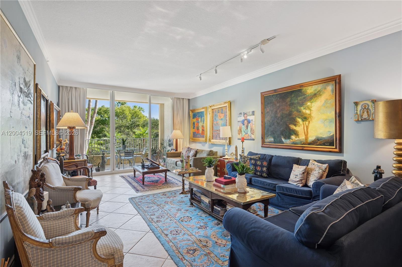 A living room features tiled floors, blue sofas, multiple framed paintings, and a balcony view — 719 Crandon Blvd # 310, Key Biscayne FL 33149, KEY BISCAYNE, FL