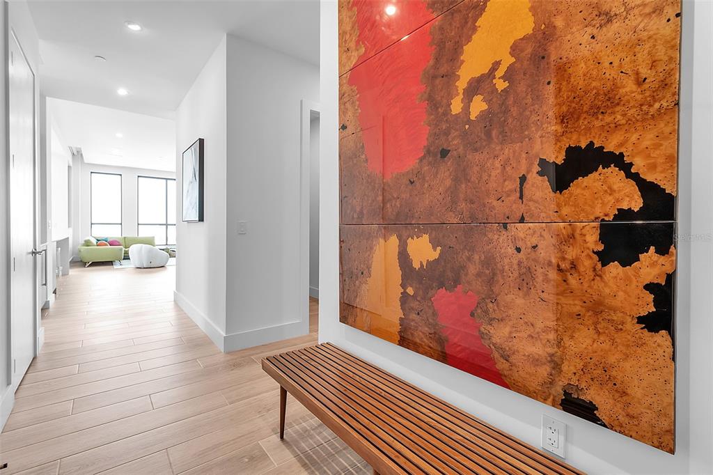 A hallway features a large abstract wall panel, a wooden bench, and light wood flooring — 33 S PALM AVENUE UNIT 701, SARASOTA, FL