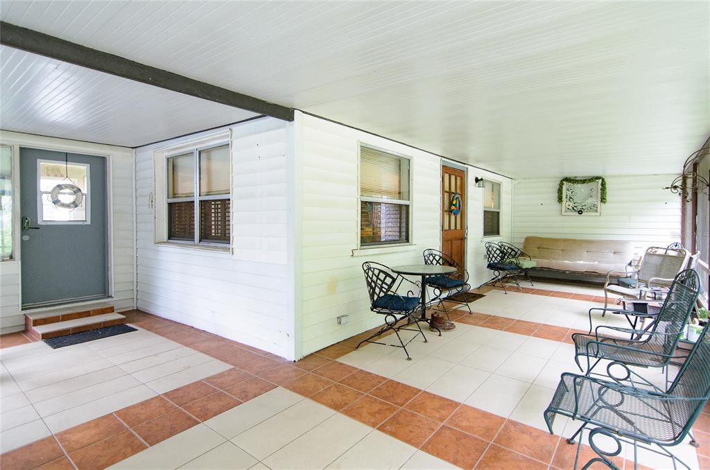 A covered patio features white siding, tile flooring, and several pieces of outdoor furniture — 257 DESOTO AVENUE, DE LEON SPRINGS, FL