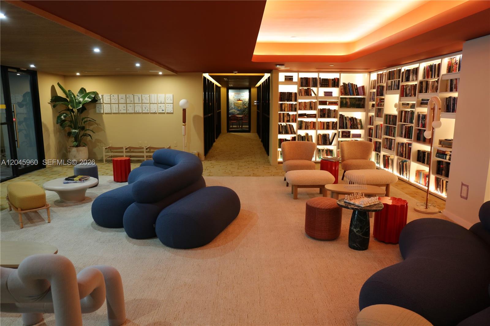 A modern lounge area features blue sculptural sofas, beige armchairs, and floor-to-ceiling bookshelves — 90 NE 32nd St # 706, Miami FL 33137, MIAMI, FL