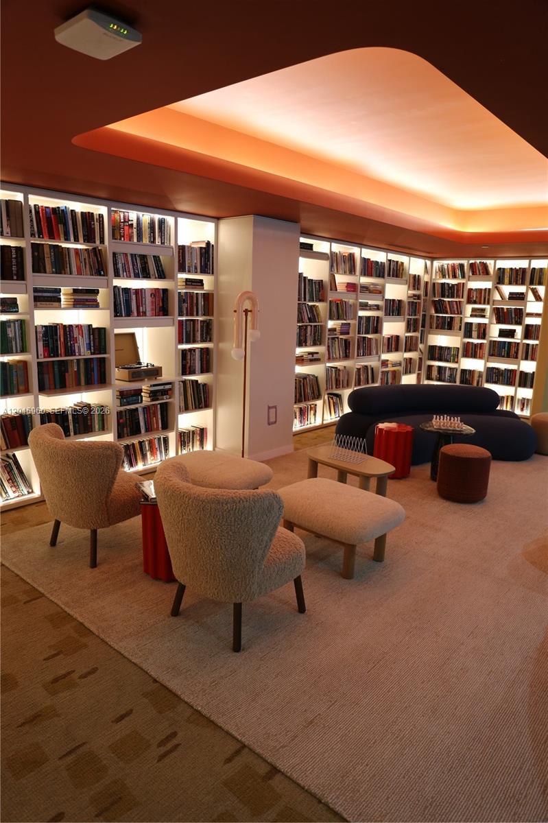 A modern library room features floor-to-ceiling bookshelves, plush seating, and a recessed orange ceiling light — 90 NE 32nd St # 706, Miami FL 33137, MIAMI, FL
