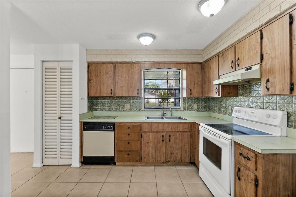 A kitchen features wood cabinets, green tile backsplash, white appliances, and light-colored floor tiles — 977 WHIPORWILL DRIVE, PORT ORANGE, FL