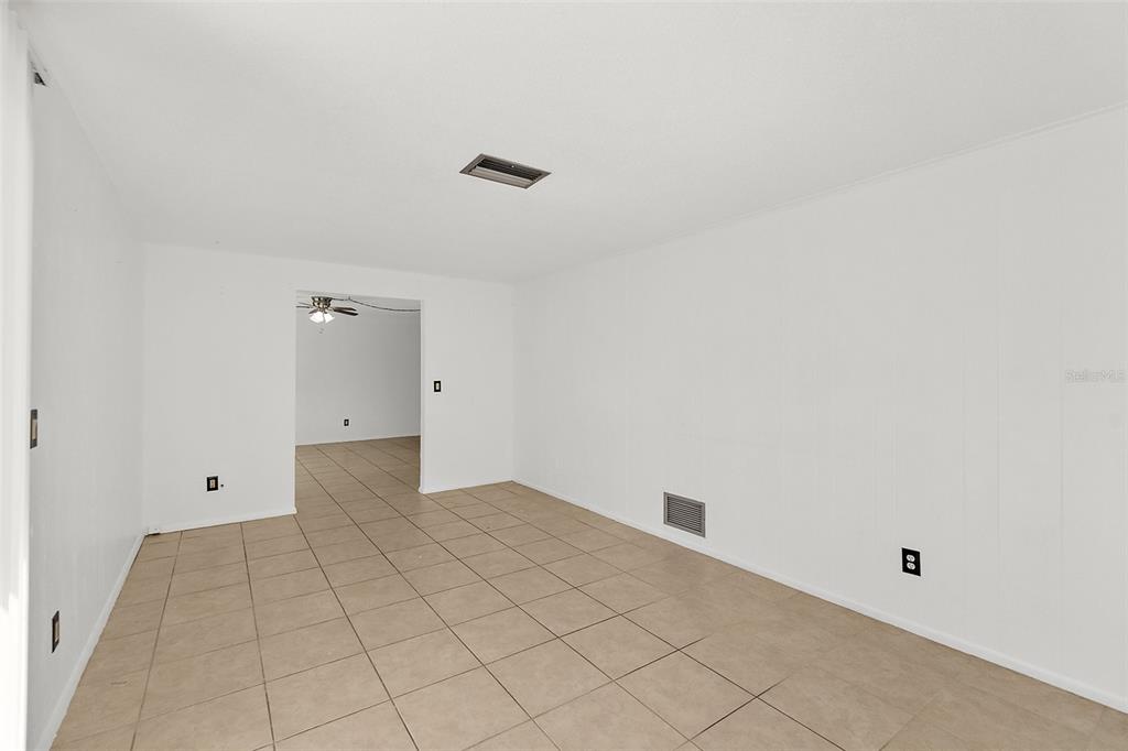 An empty room with white walls, beige tile flooring, and a doorway to another room — 977 WHIPORWILL DRIVE, PORT ORANGE, FL